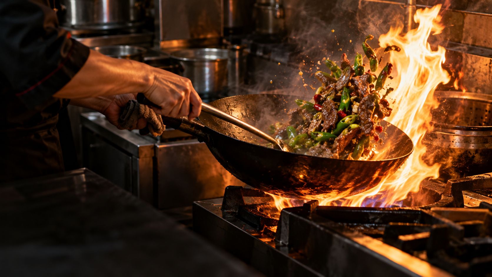 A chef tossing beef and green chillies in a wok over a roaring flame